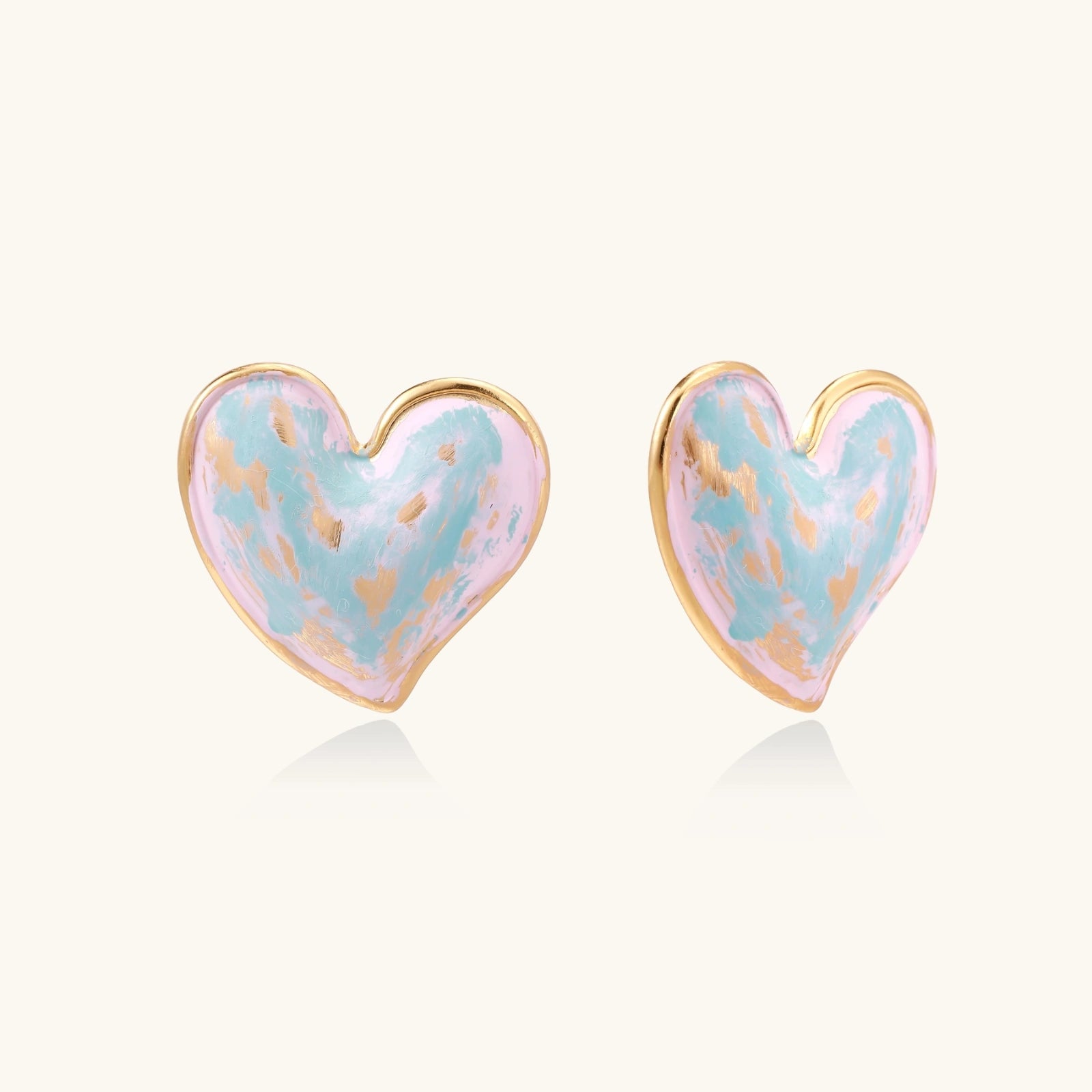 Heart-shaped stud earrings with swirled turquoise and pink enamel in gold-plated frames on cream background