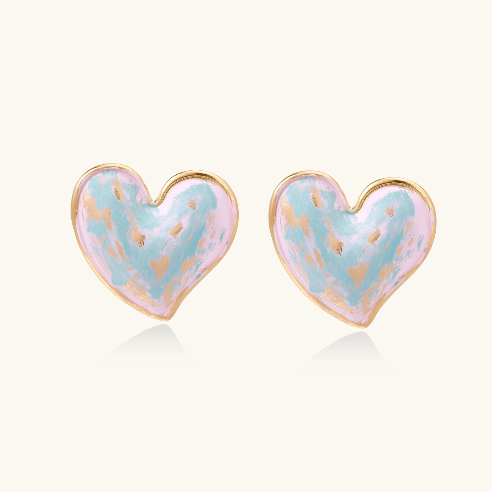 Heart-shaped stud earrings with swirled turquoise and pink enamel in gold-plated frames on cream background