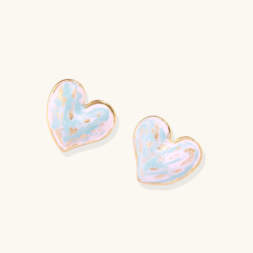 Heart-shaped stud earrings with swirled turquoise and pink enamel in gold-plated frames on cream background