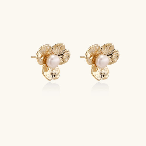 Gold-plated flower stud earrings with textured petals and centered freshwater pearl on beige background