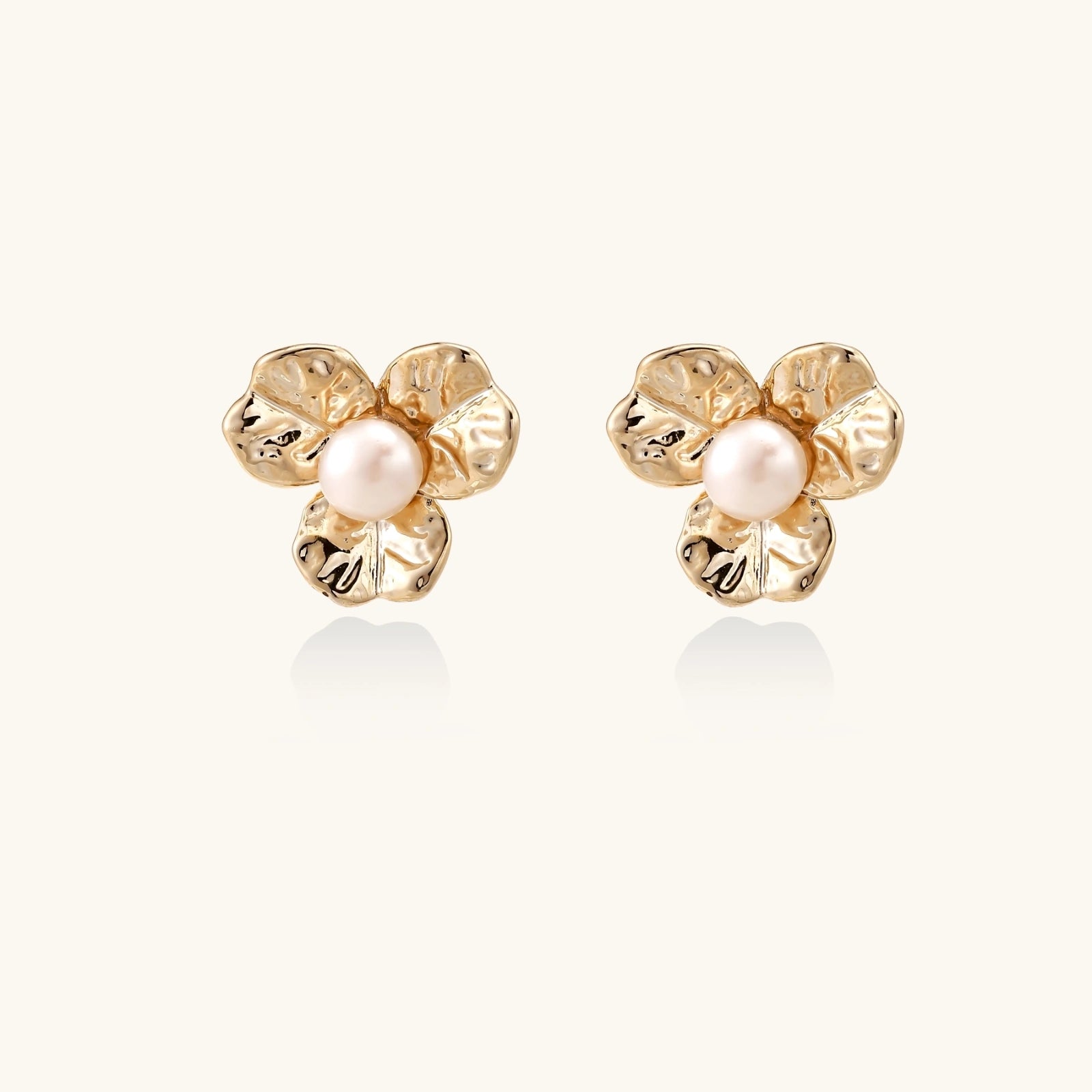 Gold-plated flower stud earrings with textured petals and centered freshwater pearl on beige background
